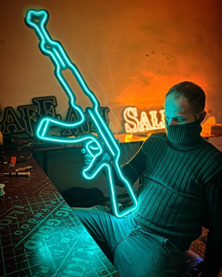 a man holding a teal colored AK-47 Neon Sign with black acrylic backing | ManhattanNeons