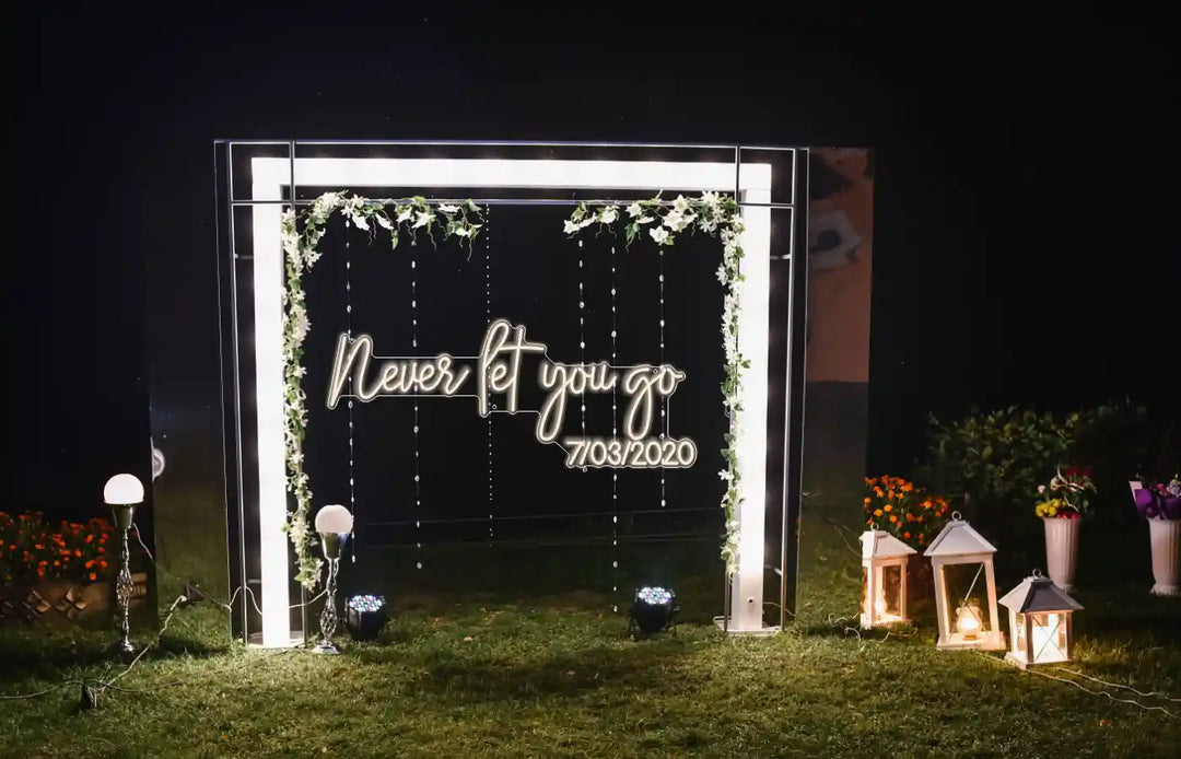 In the garden, a wedding party glows beside the Never Let You Go wedding neon sign from ManhattanNeons.com.